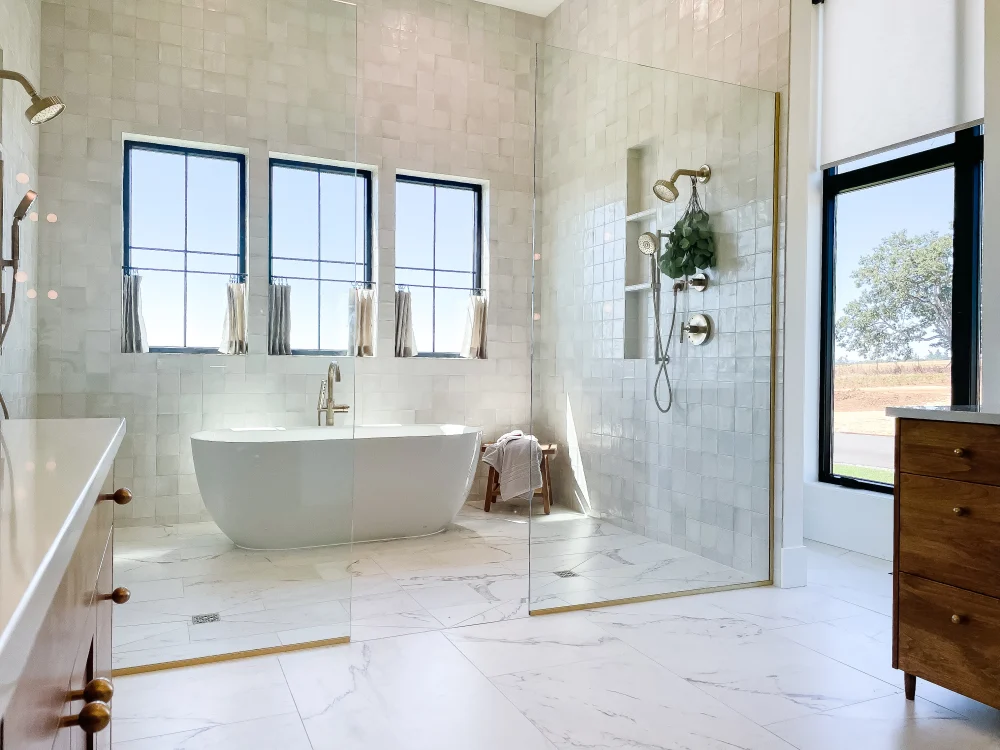 Modern bathroom featuring a freestanding white bathtub, glass shower enclosure with tile, large windows for natural light, and elegant fixtures, highlighting expert tile installation and design.
