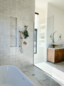 Modern bathroom featuring white tiled walls, a glass shower enclosure, and a wooden vanity with round mirror, showcasing a stylish and functional tile installation.