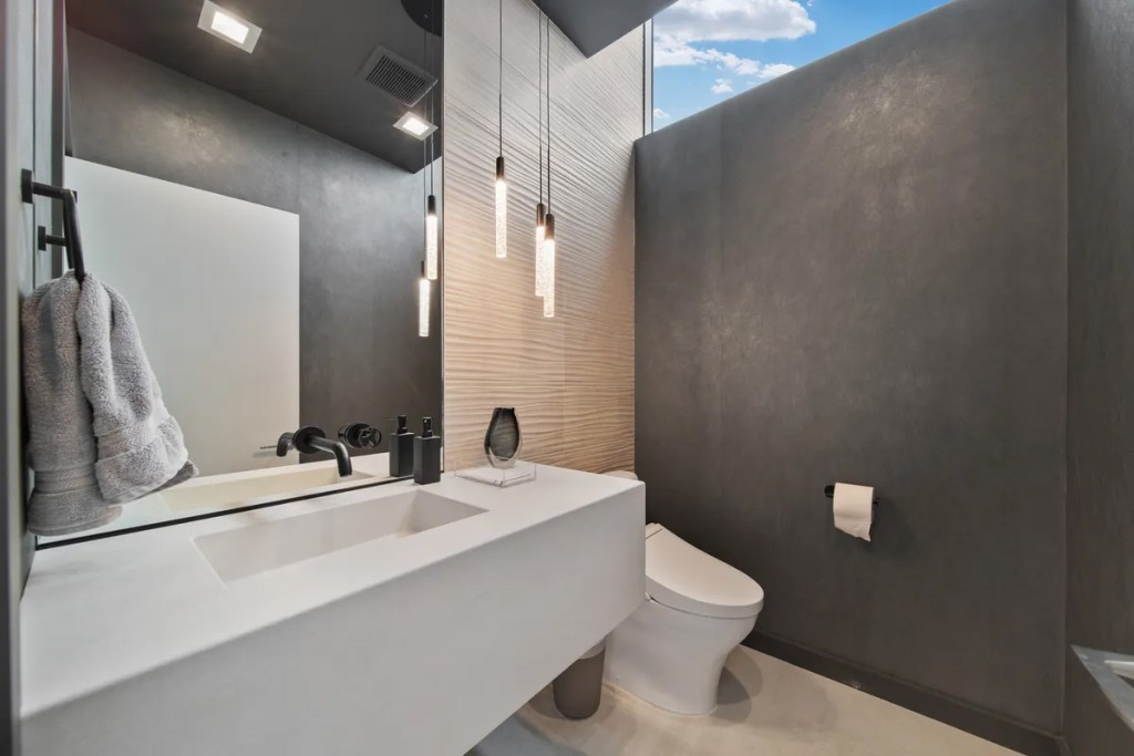 Modern bathroom with matte gray walls, floating white vanity, wall-mounted faucet, pendant lighting, and a minimalist toilet.